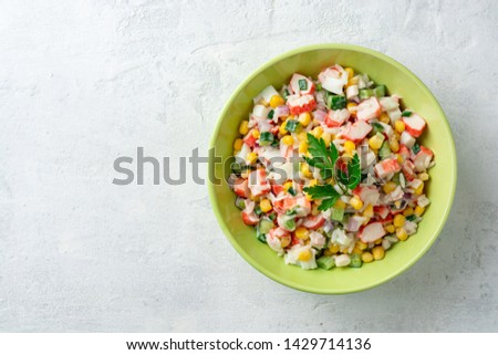 Salad with crab sticks, sweet corn, cucumbers, boiled eggs, onion and rice in bowl on concrete background. Russian cuisine. Top view. Copy space.