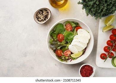 Salad with green leaves, lettuce, spinach, cherry tomatoes, mozzarella, olive oil, chilli pepper, lime juice on grey stone surface. Copy space for text. Top view
