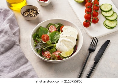 Salad with green leaves, lettuce, spinach, cherry tomatoes, mozzarella, olive oil, chilli pepper, lime juice on grey stone surface