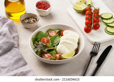 Salad with green leaves, lettuce, spinach, cherry tomatoes, mozzarella, olive oil, chilli pepper, lime juice on grey stone surface