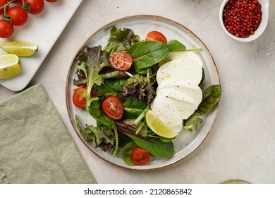 Salad with green leaves, lettuce, spinach, cherry tomatoes, mozzarella, olive oil, chilli pepper, lime juice on grey stone surface, top view