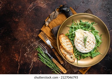 Salad with grilled Camembert cheese, arugula, toast and rosemary in a plate. Dark background. Top view. Copy space