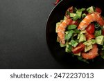 Salad of king prawns, avocado, cucumber, tomato and herbs. Black background