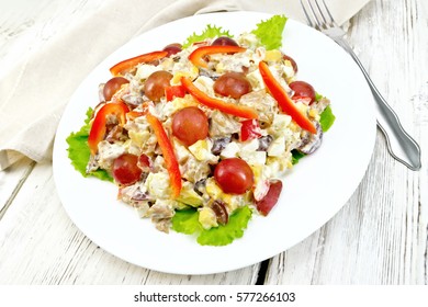 Salad of meat, salty soft feta cheese, sweet pepper, egg and grape with mayonnaise on lettuce the plate, towel and fork on the background of wooden boards - Powered by Shutterstock