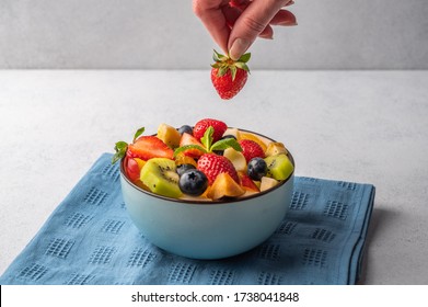 Salad from a mixture of different fruits. Woman's hand holds strawberries. Copy space for text - Powered by Shutterstock