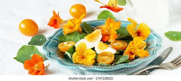 salad with nasturtium leaves and flowers of the plant. bright summer salad with edible  flowers and yellow tomatoes with egg, sunflower seeds. - Shutterstock ID 1747228022