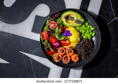 Salad With Olives, Salmon, Chia, Tomatoes, Arugula, Sesame Seeds, Endive, Mozzarella, Avocado, Beans, Violet Flower In A Plate On A Background With A Letter