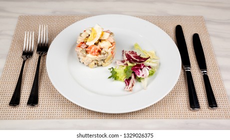 Salad Olivier with egg and cabbage on a white plate and cutlery.