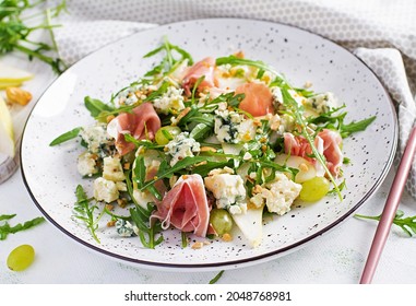 Salad of pear, blue cheese, grape, prosciutto, arugula and nuts with spicy dressing on a light background. Healthy eating.