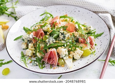 Salad of pear, blue cheese, grape, prosciutto, arugula and nuts with spicy dressing on a light background. Healthy eating.