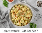 Salad of potatoes, eggs, bacon and fresh herbs with mayonnaise and yogurt dressing in a bowl on a gray concrete background