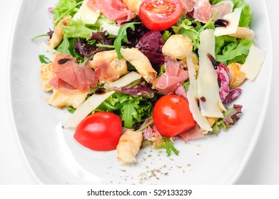 Salad with prosciutto, parmigiano, fresh cherry tomato, lettuce and ruccola, served at white plate