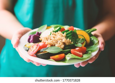 Salad quinoa seeds with vegetables on plate holding by woman hand, Healthy vegan food