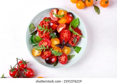 Salad with red, black and yellow cherry tomatoes, arugula and basil dressed with black salt and olive oil served on wheat straw plate. Top view - Powered by Shutterstock