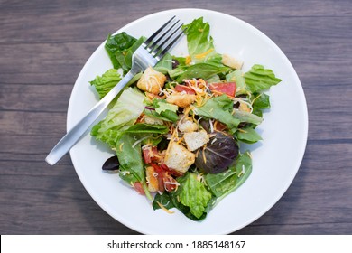 Salad Of Romaine Lettuce, Croutons, Shredded Cheddar Cheese, And Tomato On A White Plate On A Wooden Table