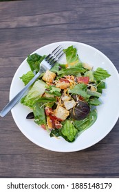 Salad Of Romaine Lettuce, Croutons, Shredded Cheddar Cheese, And Tomato On A White Plate On A Wooden Table