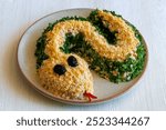 Salad with shrimps, egg, chicken, cheese and parsley in shape of green Snake as symbol of Chinese new year on a plate on a white table. Creative design for party.