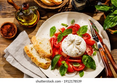 Salad with Tomatoes and Burrata cheese with basil and olive oil on wooden background - Shutterstock ID 1912178539