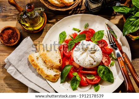 Salad with Tomatoes and Burrata cheese with basil and olive oil on wooden background