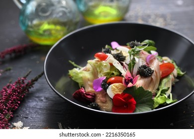Salad with vegetables, fresh fish, caviar and quail egg, decorated with edible flowers. Fish salad in a black bowl, close up.