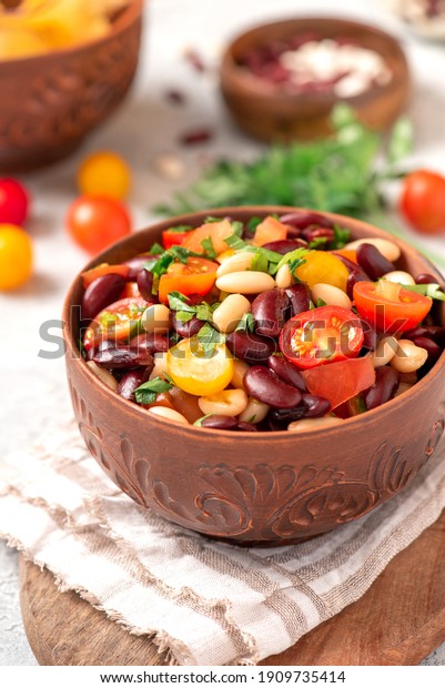 Salad of white and red beans,\
tomatoes and herbs in a ceramic bowl close-up. Tasty vegan\
food