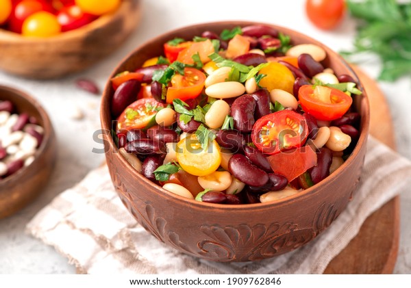Salad of white and red beans,\
tomatoes and herbs in a ceramic bowl close-up. Tasty vegan\
food