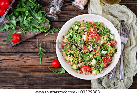 Salads with quinoa,  arugula, radish, tomatoes and cucumber in bowl on  wooden background.  Healthy food, diet, detox and vegetarian concept. Top view. Flat lay