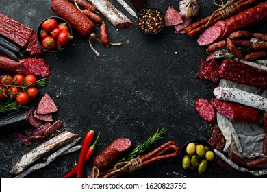 Salami and snacks. Sausage Fouet, sausages, salami, paperoni, on a black stone background. Top view. Free space for your text.