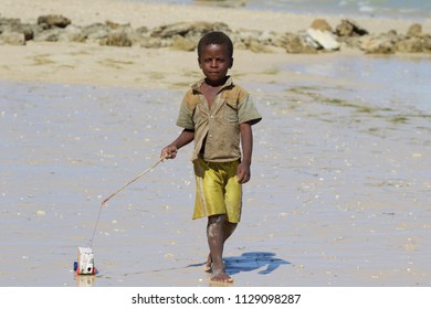 SALARY BAY, MADAGASCAR - AUGUST 2017: A Little African Child Plays With A Self-made Toy Car Built With An Orange Juice Box On The Salary Bay Beach In The Southwest Of Madagascar