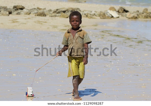 SALARY BAY,\
MADAGASCAR - AUGUST 2017: a little African child plays with a\
self-made toy car built with an orange juice box on the salary bay\
beach in the southwest of\
Madagascar