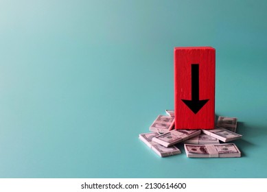 Salary reduction, recession, financial crisis. Red wooden cube with downward arrow and banknotes.
