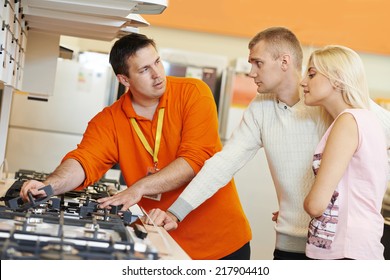 Sale Assistant Demonstrating Cooker Stove To Young Family In Home Appliance Shopping Mall Supermarket