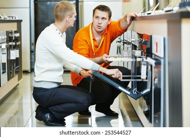 Sale Assistant Demonstrating Cooker Stove To Young Family In Home Appliance Shopping Mall Supermarket