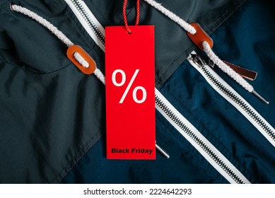 Sale, black friday concept. Red tag with Percentage discount sign and text Black Friday hanging on dark blue jacket in clothing store, close-up.
