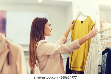 Sale, Clothes , Shopping, Fashion And People Concept - Happy Young Woman Choosing Between Two Shirts In Mall Or Clothing Store