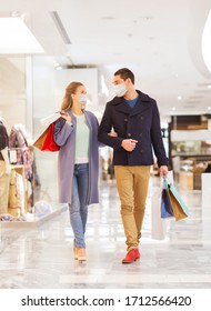 Sale, Consumerism And Pandemic Concept - Happy Young Couple Wearing Face Protective Medical Mask For Protection From Virus Disease With Shopping Bags Walking And Talking In Mall