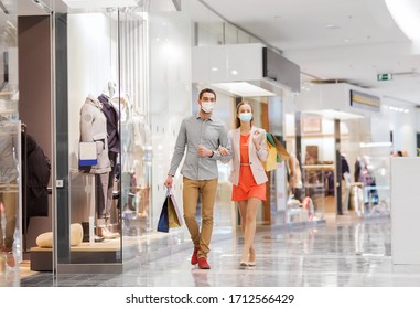 sale, consumerism and pandemic concept - happy young couple wearing face protective medical mask for protection from virus disease with shopping bags walking in mall