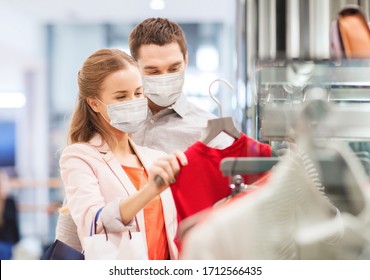 Sale, Consumerism And Pandemic Concept - Happy Young Couple Wearing Face Protective Medical Mask For Protection From Virus Disease With Shopping Bags In Mall