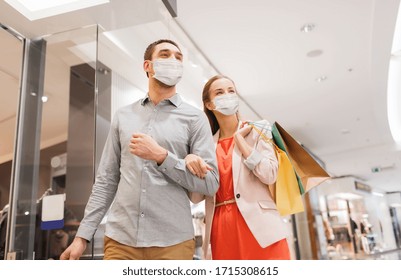 Sale, Consumerism And Pandemic Concept - Happy Young Couple Wearing Face Protective Medical Mask For Protection From Virus Disease With Shopping Bags In Mall