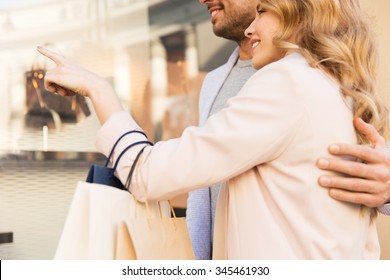 sale, consumerism and people concept - close up of happy couple with shopping bags looking at shop window in city