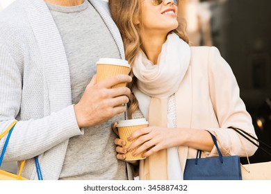 Sale, Consumerism And People Concept - Close Up Of Happy Couple With Shopping Bags And Coffee Paper Cups At Shop Window On City Street