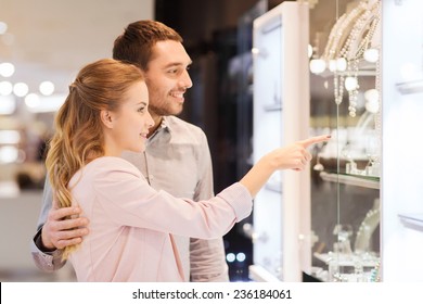 Sale, Consumerism And People Concept - Happy Couple Pointing Finger To Shopping Window At Jewelry Store In Mall