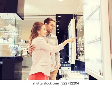 Sale, Consumerism And People Concept - Happy Couple Pointing Finger To Shopping Window At Jewelry Store In Mall