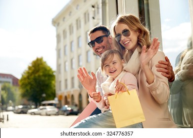 Sale, Consumerism And People Concept - Happy Family With Little Child And Shopping Bags Waving Hands At Shop Window In City