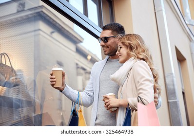 Sale, Consumerism And People Concept - Happy Couple With Shopping Bags And Coffee Paper Cups Looking At Shop Window In City