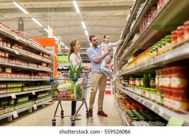 Sale, Consumerism And People Concept - Happy Family With Child And Shopping Cart Buying Food At Grocery Store Or Supermarket