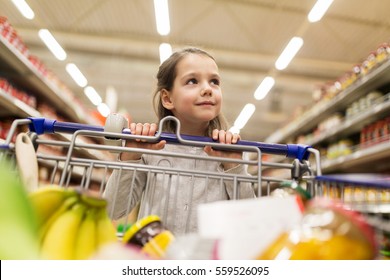 sale, consumerism and people concept - happy little girl with food in shopping cart at grocery store