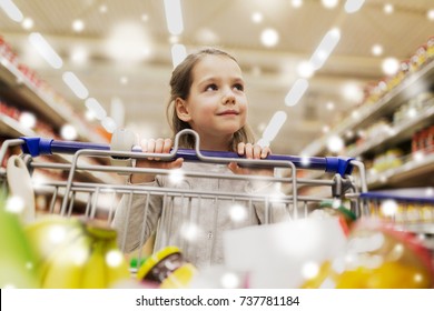sale, consumerism and people concept - happy little girl with food in shopping cart at grocery store or supermarket over snow