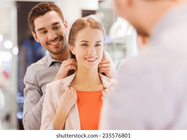 Sale, Consumerism, Presents, Holidays And People Concept - Happy Couple Trying Golden Pendant On At Jewelry Store In Mall