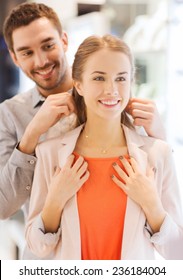 Sale, Consumerism, Presents, Holidays And People Concept - Happy Couple Trying Golden Pendant On At Jewelry Store In Mall